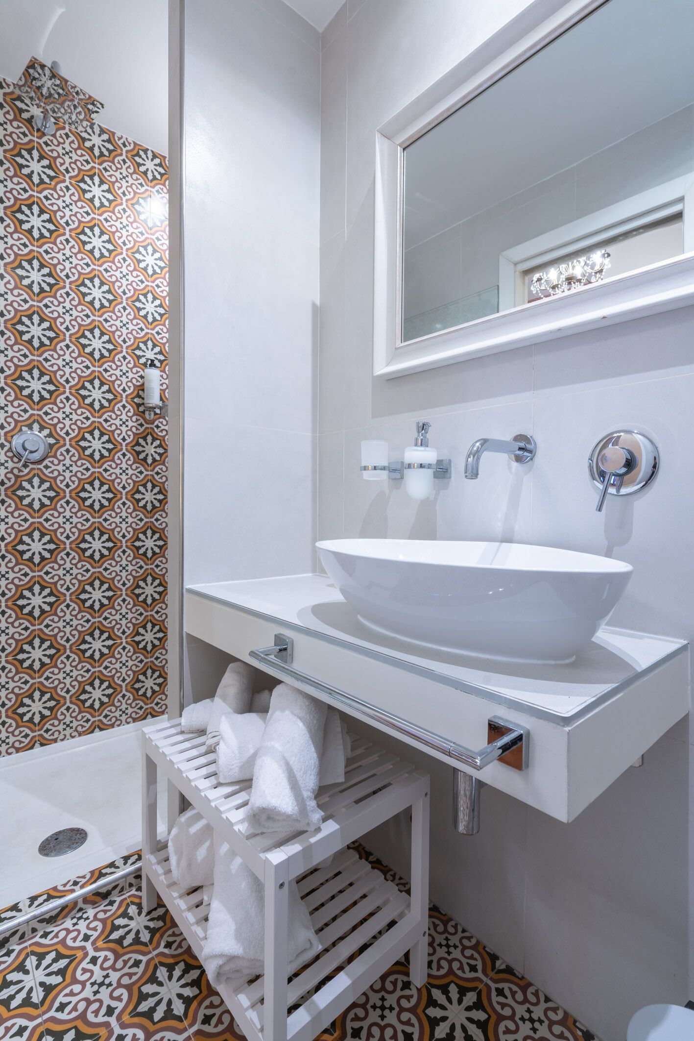A bathroom with a white sink, a mirror, and a patterned shower wall.