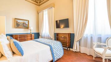 Habitación de hotel con cama, televisión, cómoda, una silla y un cuadro en la pared.