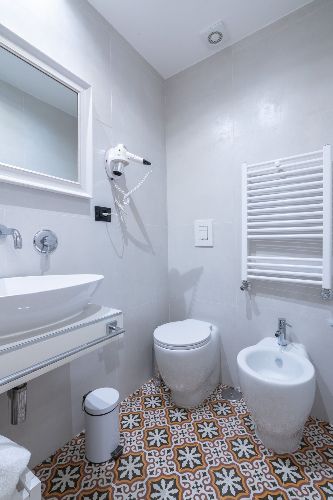 Een badkamer met een wit wastafel, toilet en bidet, een spiegel en een vloer met een patroon.