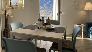 A dining area with a table set for two, a vase with flowers, and a view of mountains through a window. - Apartment for 2 persons, balcony and garden, 500m to the lake (Lombardia)