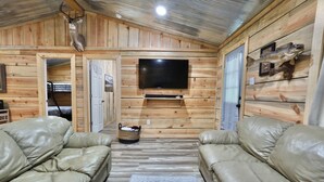 A wooden cabin interior with leather sofas, a mounted television, and a ceiling-mounted deer head.
