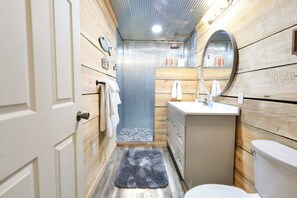 A compact bathroom with wooden walls, a white sink, and a round mirror.