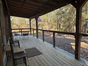 A covered outdoor seating area with wooden benches and tables, overlooking a forested area.