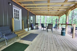 A covered porch with a wooden ceiling, a gray door, and a seating area with two chairs and a sofa.