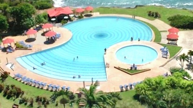 Uma grande piscina circular com vários níveis de degraus para entrar na água, cercada por espreguiçadeiras e guarda-sóis.
