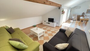 Una sala de estar con un sofá verde, un sofá negro, una mesa de centro blanca y un televisor sobre un mueble blanco.