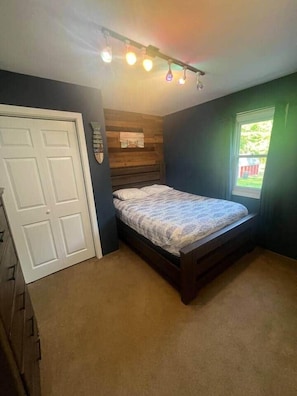 Un dormitorio con una cama, una puerta, un ventanal y una lámpara fijada a la pared.