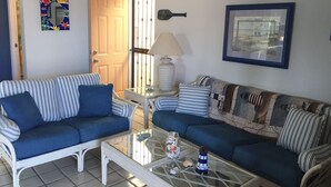 Una sala de estar con dos sofás azules, una mesa de centro de vidrio y una puerta con reja de metal.
