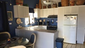 Una cocina compacta con armarios blancos, una isla central, un lavamanos y un refrigerador.