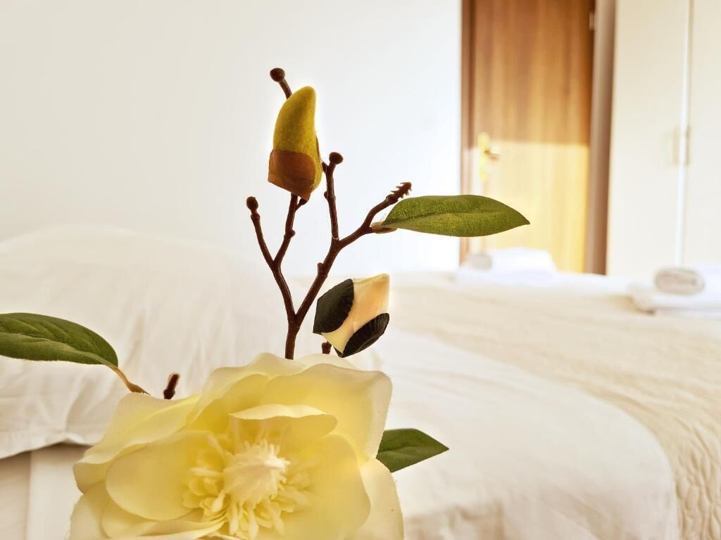 Un lit avec une literie blanche, une seule fleur jaune et une feuille verte.