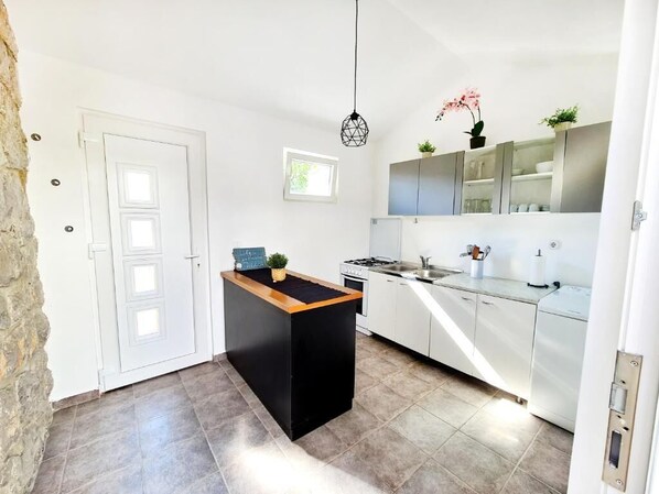 Una cocina moderna con una isla central, armarios blancos y una pared de piedra.