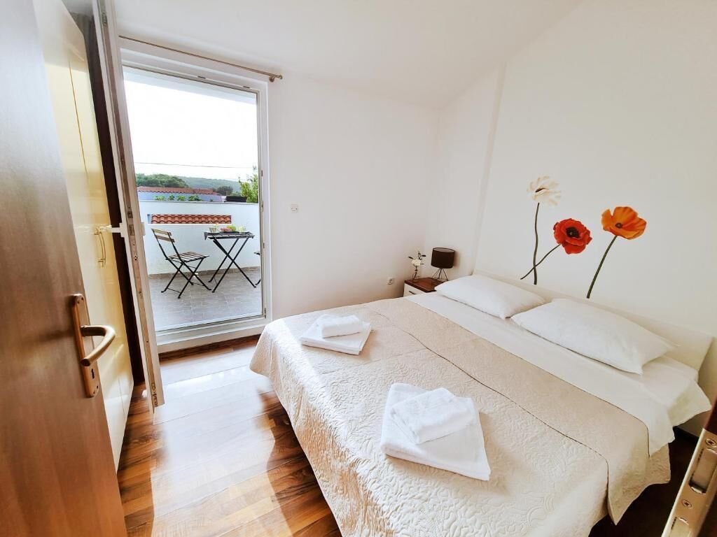 A bedroom with a bed, a nightstand, a lamp, and a view of the outside balcony.