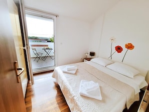 Un dormitorio con cama, mesita de noche, lámpara y vistas al balcón.