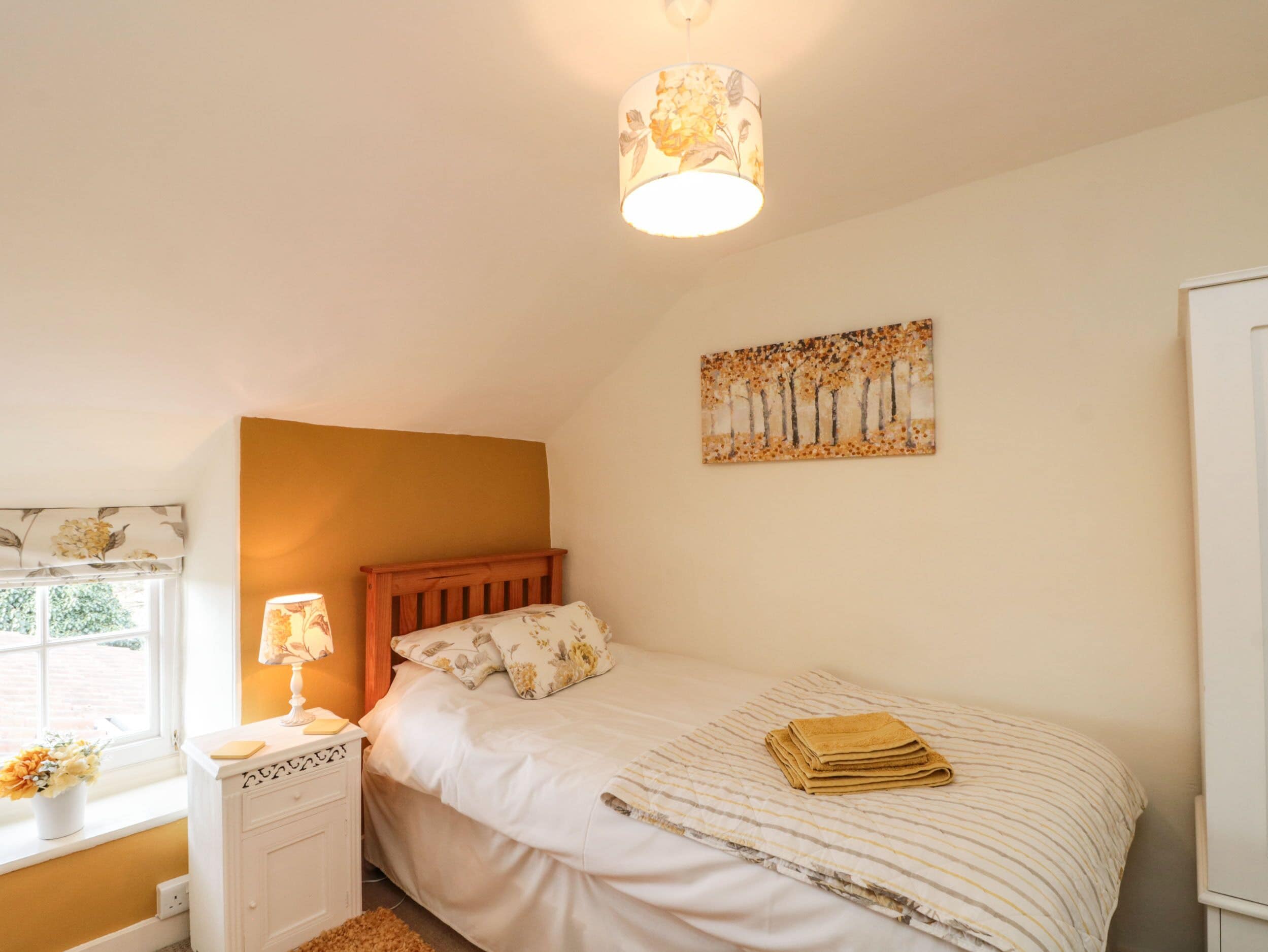 A bedroom with a bed, nightstand, lamp, and a painting on the wall.