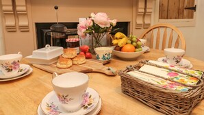 A dining table set with floral-patterned cups, saucers, biscuits, a fruit bowl, and a wicker basket. - 12 Castlegate (Pickering)