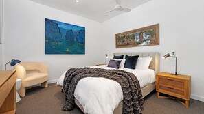 A bedroom with a bed, a chair, a nightstand, a desk, and two paintings on the wall. - The View by Experience Jervis Bay (Huskisson)