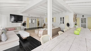 A spacious living area with a high ceiling, a large flat-screen TV, a dining table with chairs, and a sofa.