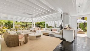 A spacious living area with a white ceiling, a sofa set, a round coffee table, and a kitchen area with a fan.