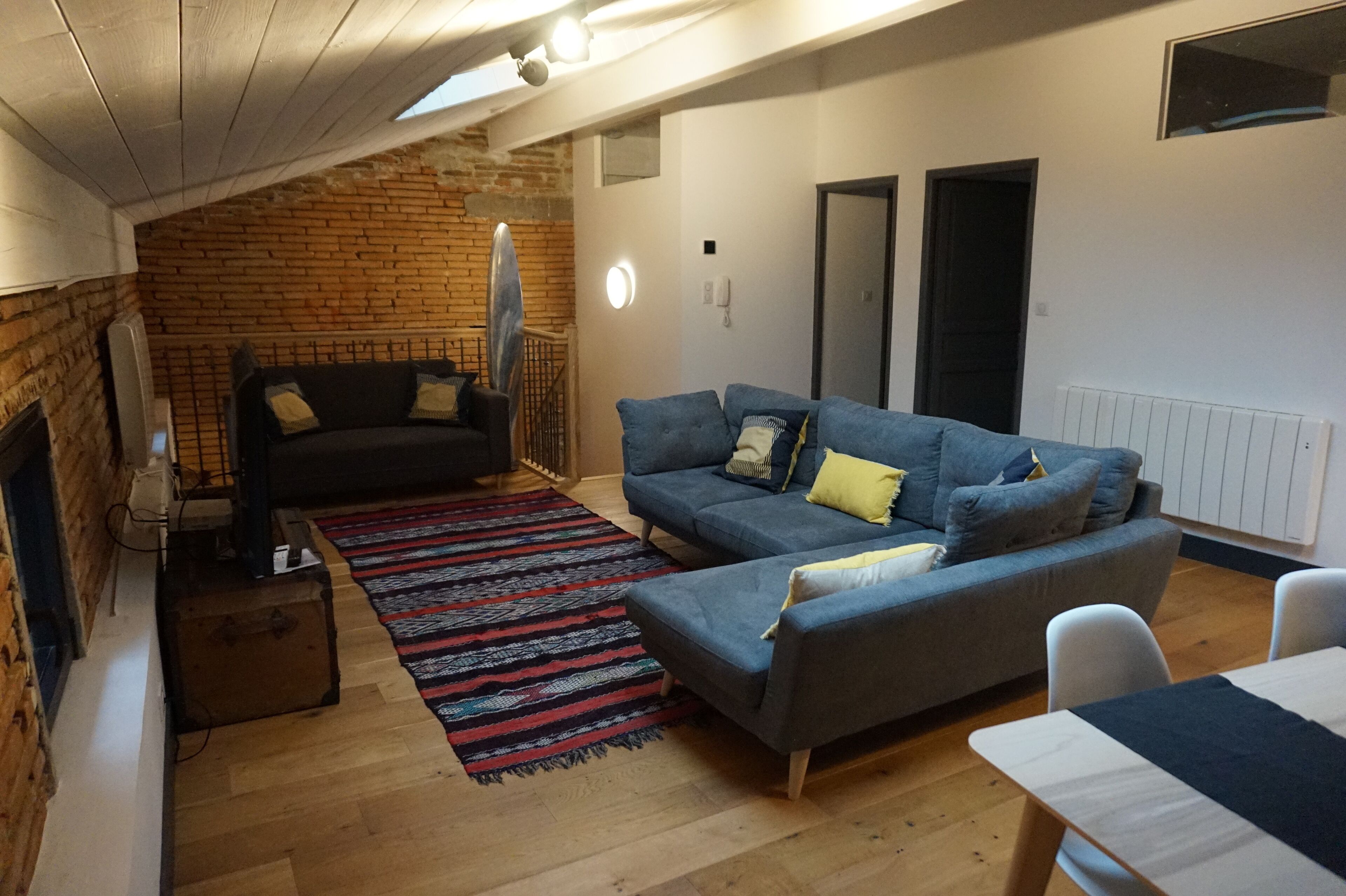 A cozy living room with a brick wall, a blue sofa, a patterned rug, and a small table.