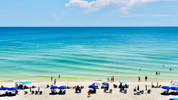 A beach with clear turquoise water, people walking, and beach umbrellas. - Gulf-Front Condo with Spectacular views on the 5th Floor! (Gulf Shores)