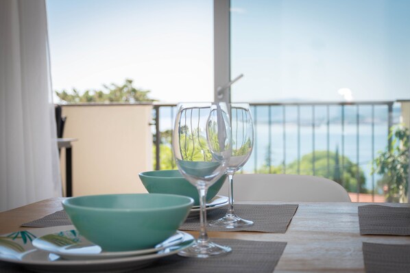 Una mesa de comedor con vista al mar, dos copas de vino y un cuenco color turquesa.
