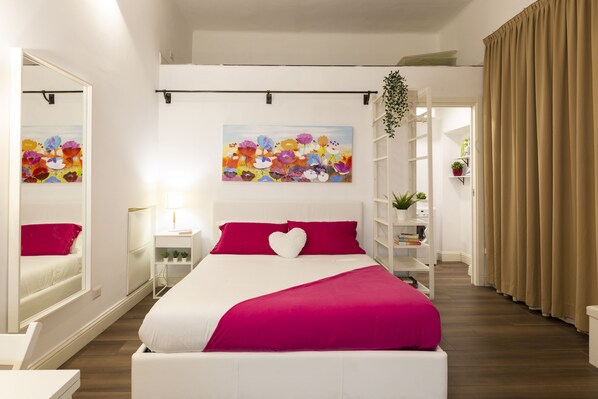 Une chambre moderne avec un grand lit, un miroir, un tableau coloré et une plante.