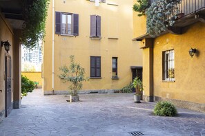 Une cour avec un bâtiment jaune, un sol pavé de pierres et des plantes en pot.