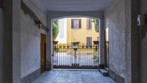 Une entrée pavée de pierres, avec un portail en métal qui mène à un bâtiment jaune.
