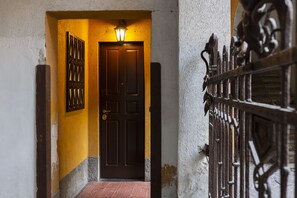 Un couloir étroit avec une porte en bois sombre, un portail en métal et un luminaire fixé au mur.