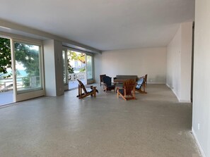 A spacious room with large windows, a dining area with wooden chairs, and a view of the outdoors.