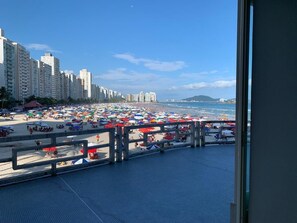 Una playa con muchos sombrillas y gente, un paseo marítimo con barandilla y edificios altos al fondo.