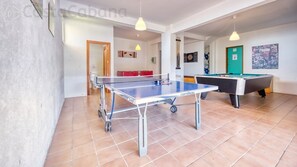A room with a ping pong table, a pool table, and a sofa.