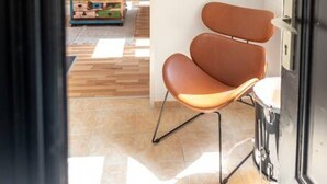 A modern interior with a brown leather chair, a wooden floor, and a hanging light fixture.