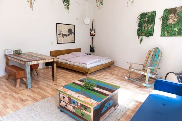 Une chambre avec un lit en bois, un bureau, une table basse aux couleurs vives et une chaise bleue.