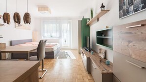 A modern, well-lit room with a wooden dining table, a sofa, and a TV mounted on a green shelf.