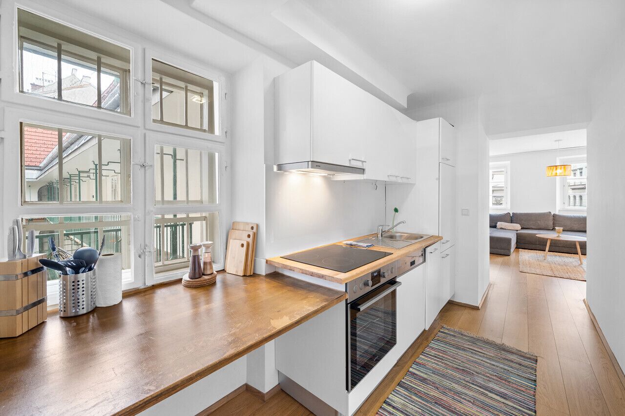 A modern kitchen with a wooden countertop, built-in oven, and white cabinetry.