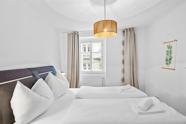 A hotel room with a bed, curtains, a hanging plant, and a window.
