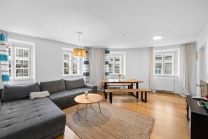 A modern living room with a grey sectional sofa, a round coffee table, a wooden dining table, and a hanging light fixture.