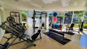 Une salle de sport équipée de divers appareils d’exercice, d’un banc et offrant une vue sur l’extérieur grâce à de grandes fenêtres.