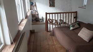 Ein Schlafzimmer mit schrägverdeckter Decke, Holzboden, einem Bett mit Kissen, einem Heizkörper, einem Fenster und einer Leiter.
