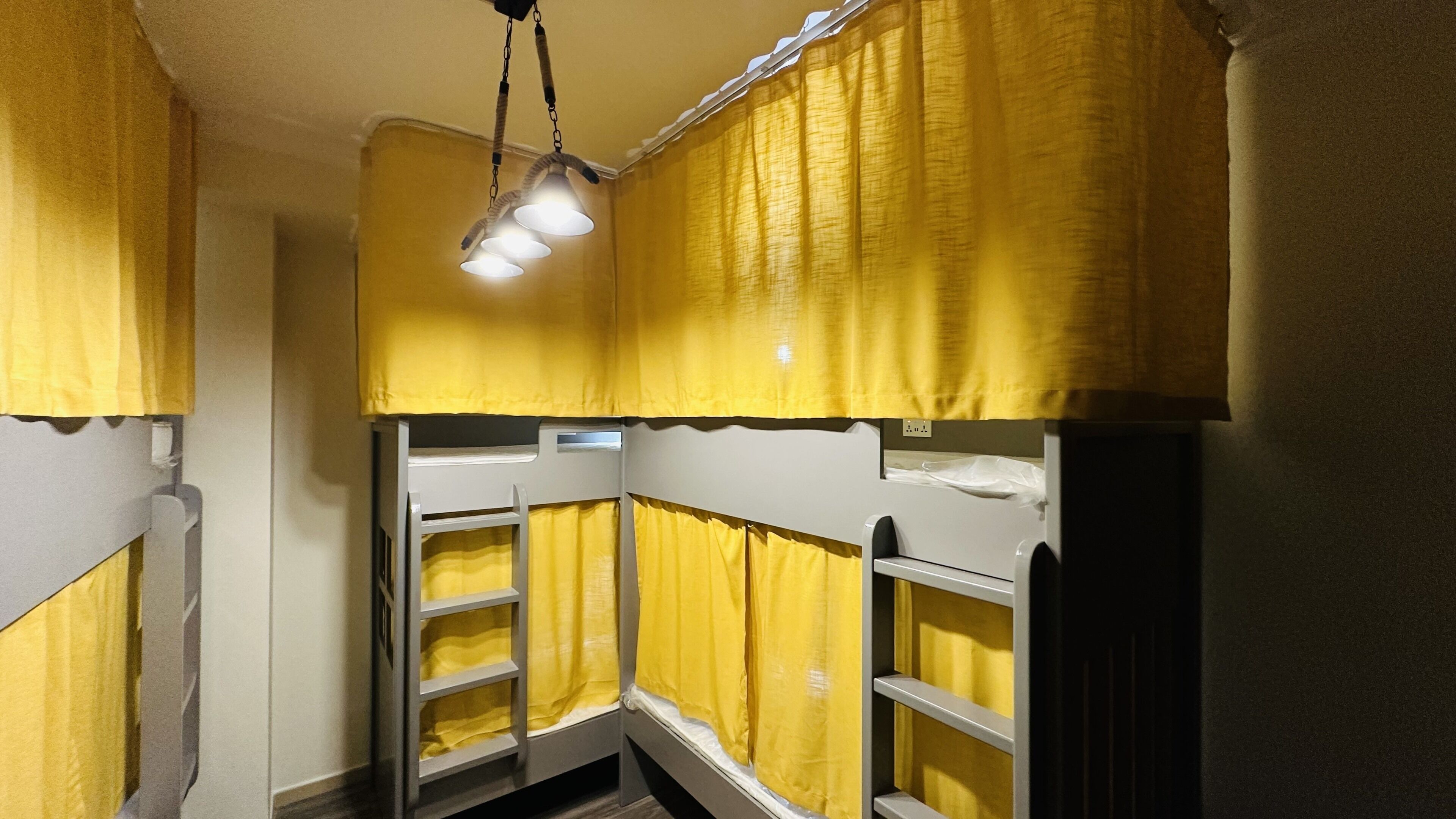 Habitación con literas, cortinas amarillas y una lámpara colgante.