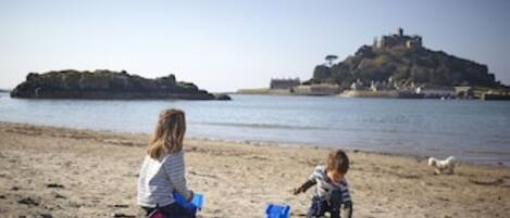 Two children playing on a sandy beach with a castle-like structure in the background.