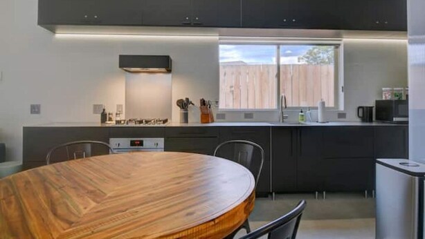 A modern kitchen with dark cabinets, a wooden dining table, and a window providing a view of the outside. - Private modern hideaway in downtown Albuquerque. (Albuquerque)