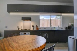 A modern kitchen with dark cabinets, a wooden dining table, and a window providing a view of the outside.