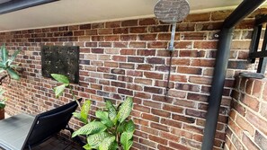Pared de maó amb una placa de metall, una cadira negra i plantes verdes.
