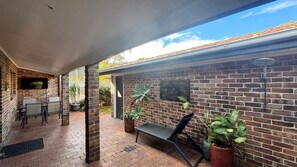 A covered patio with brick walls, a table, chairs, and potted plants.