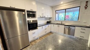 A modern kitchen with stainless steel appliances, white cabinetry, and a large window with a view of greenery.