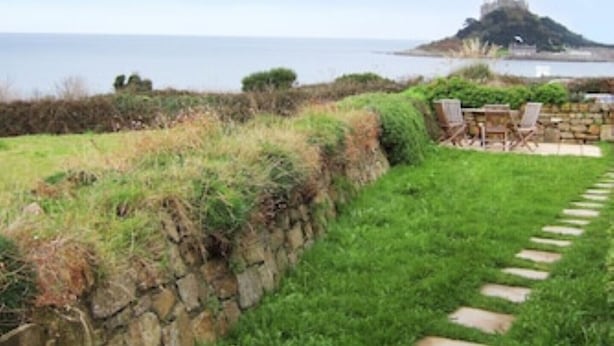 A coastal garden with a stone wall, a paved pathway, and outdoor furniture.