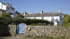 A stone wall with a blue gate, a white building with a grey roof, and a clear blue sky.