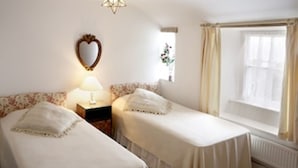 A room with two single beds, a nightstand with a lamp, a mirror, and a window with curtains.